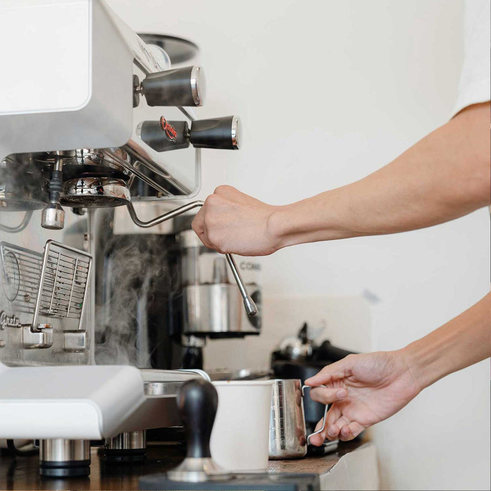 Person making coffee using an espresso machine in a kitchen setting.